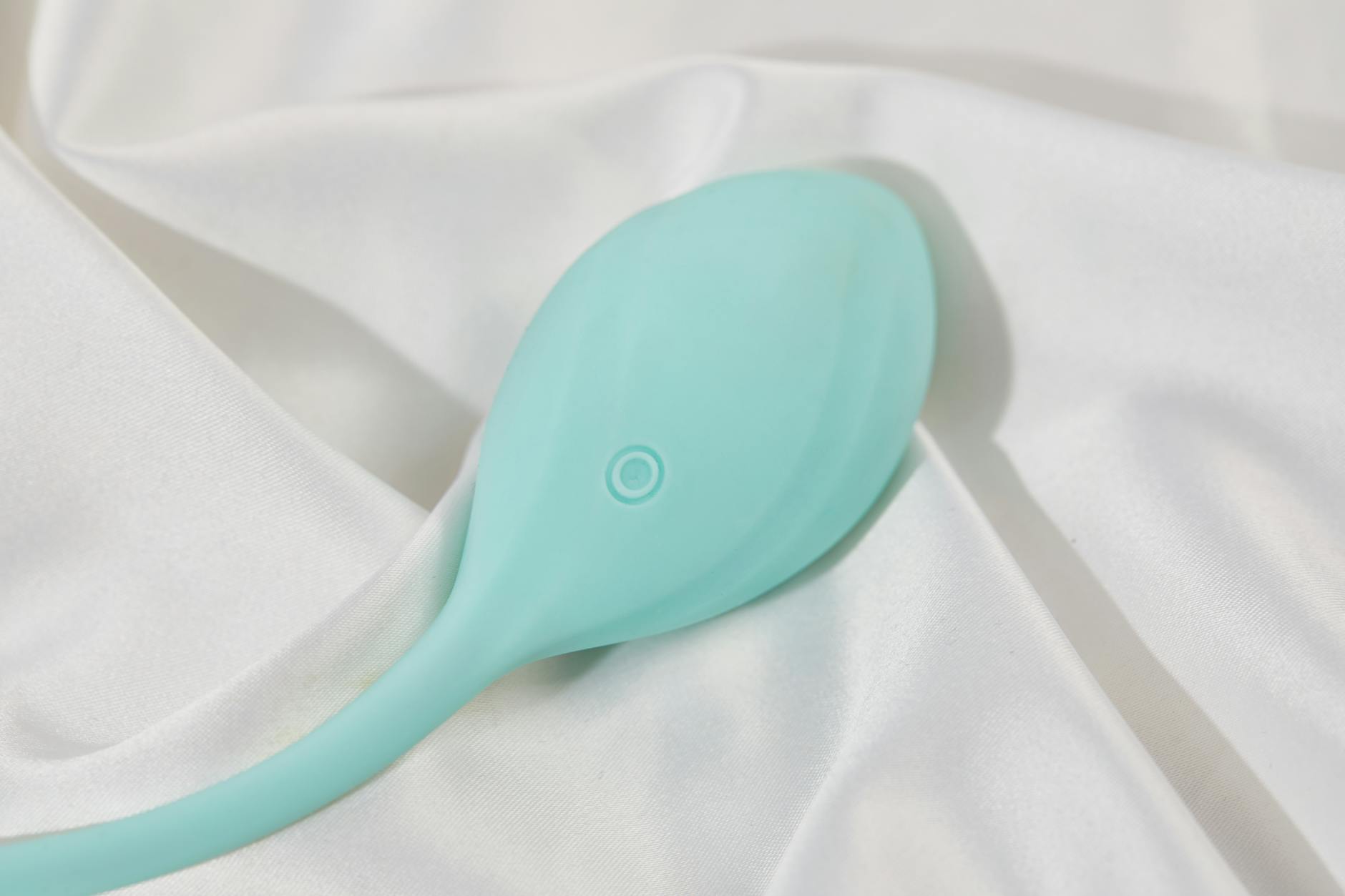 A sleek teal lemon vibrator resting on soft white silk fabric