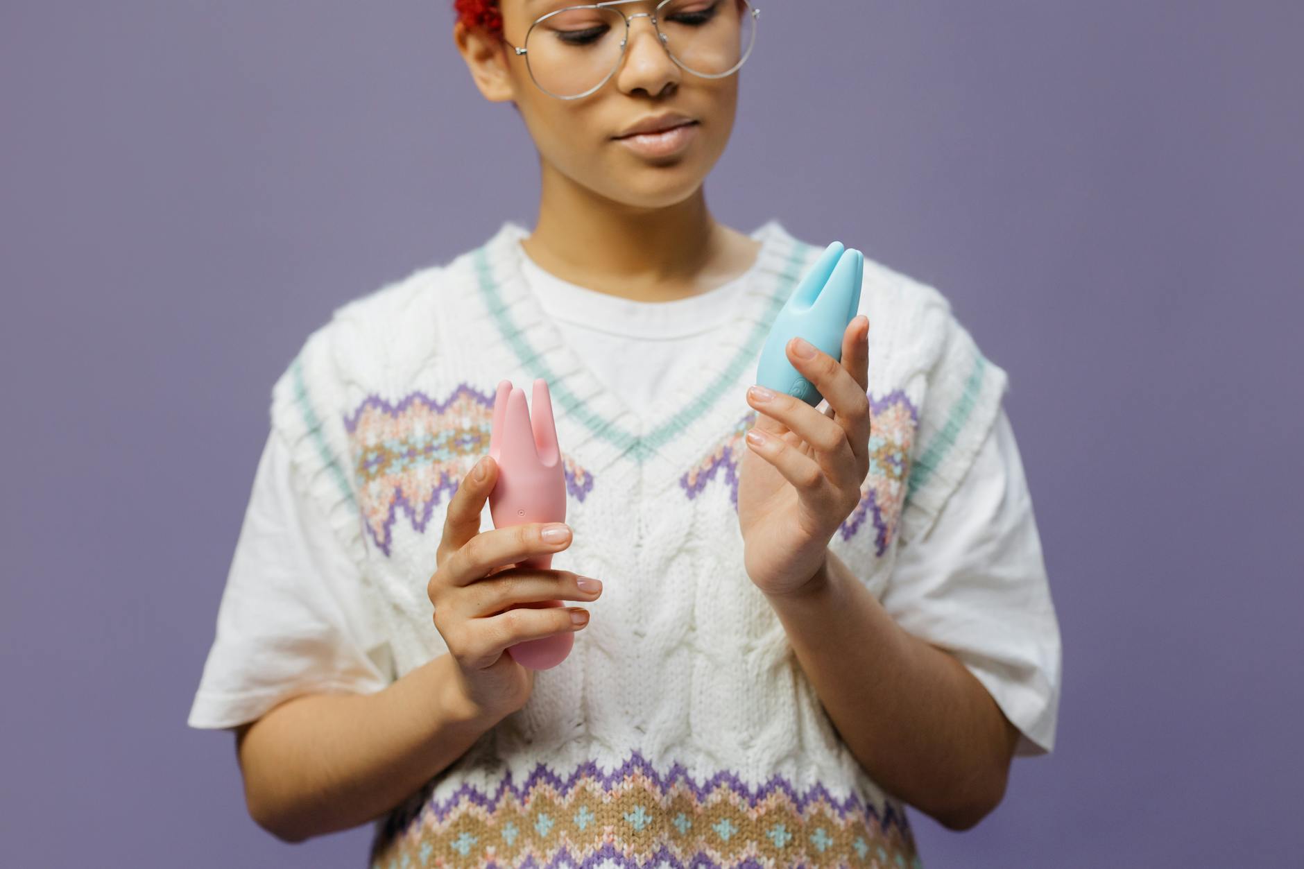 Person holding multiple silicone vibrators in different colors and designs, comparing different clitoral toy options.
