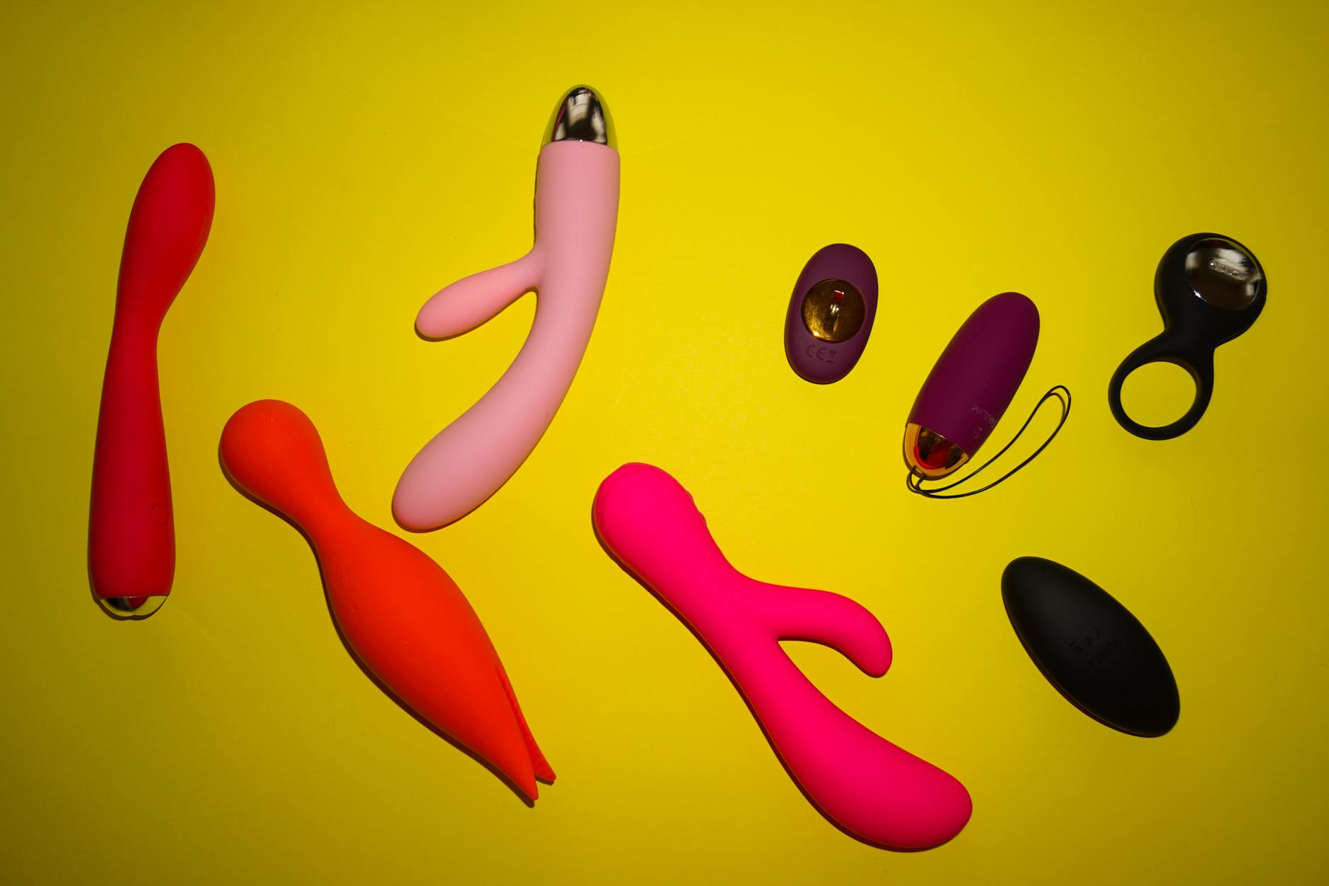 Colorful sex toys displayed on bright yellow surface, emphasizing design and variety